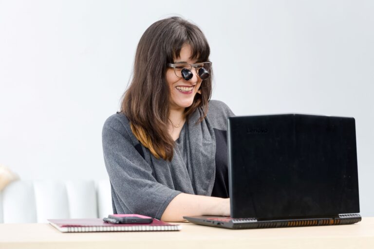 Woman typing on a laptop wearing low vision glasses