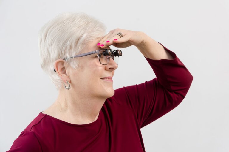 A woman wearing bioptic telescope glasses using her hand as a visor and looking into the distance
