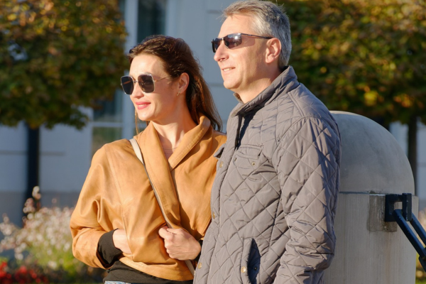 A woman and man standing at a street corner in sunglasses